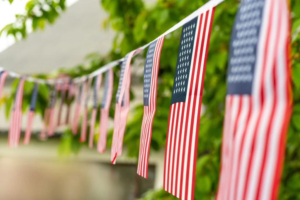 Strings of small American flags hanging as bunting among green leaves