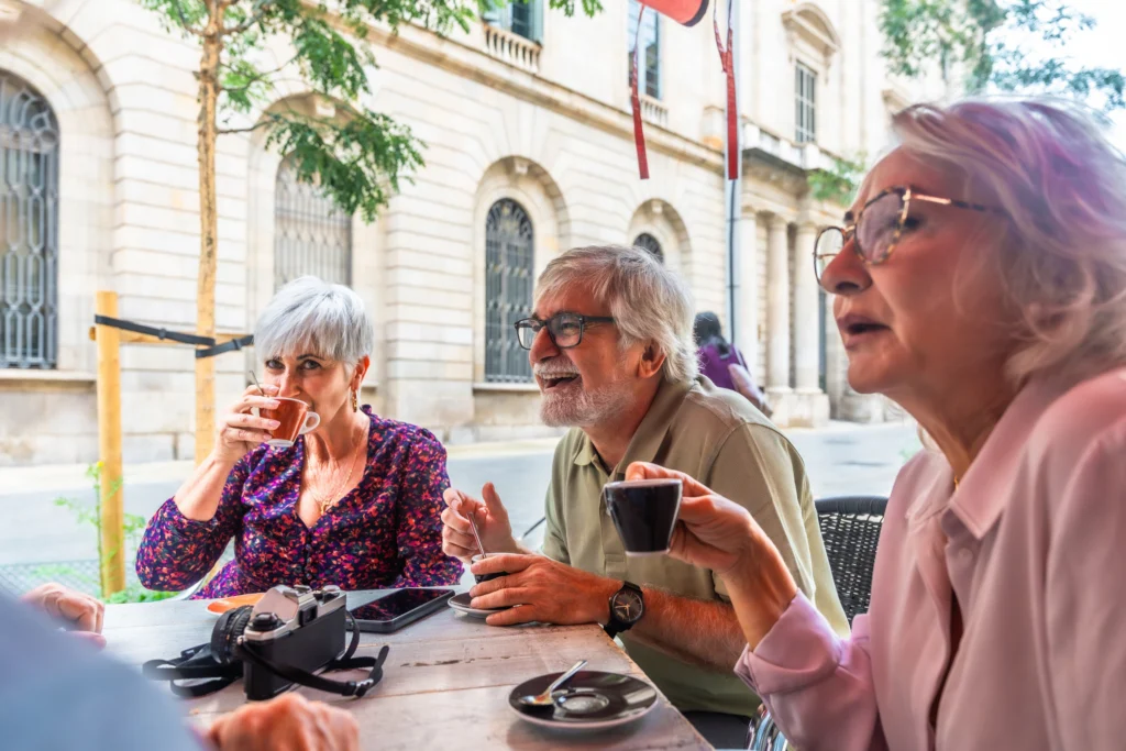 Three older adults chatting over coffee at an outdoor café table