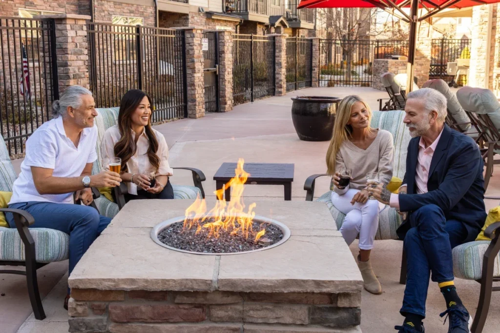 Four people gathered with drinks around an outdoor fire pit