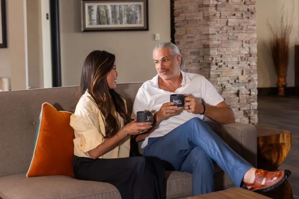 Man and woman seated on a sofa holding mugs and talking