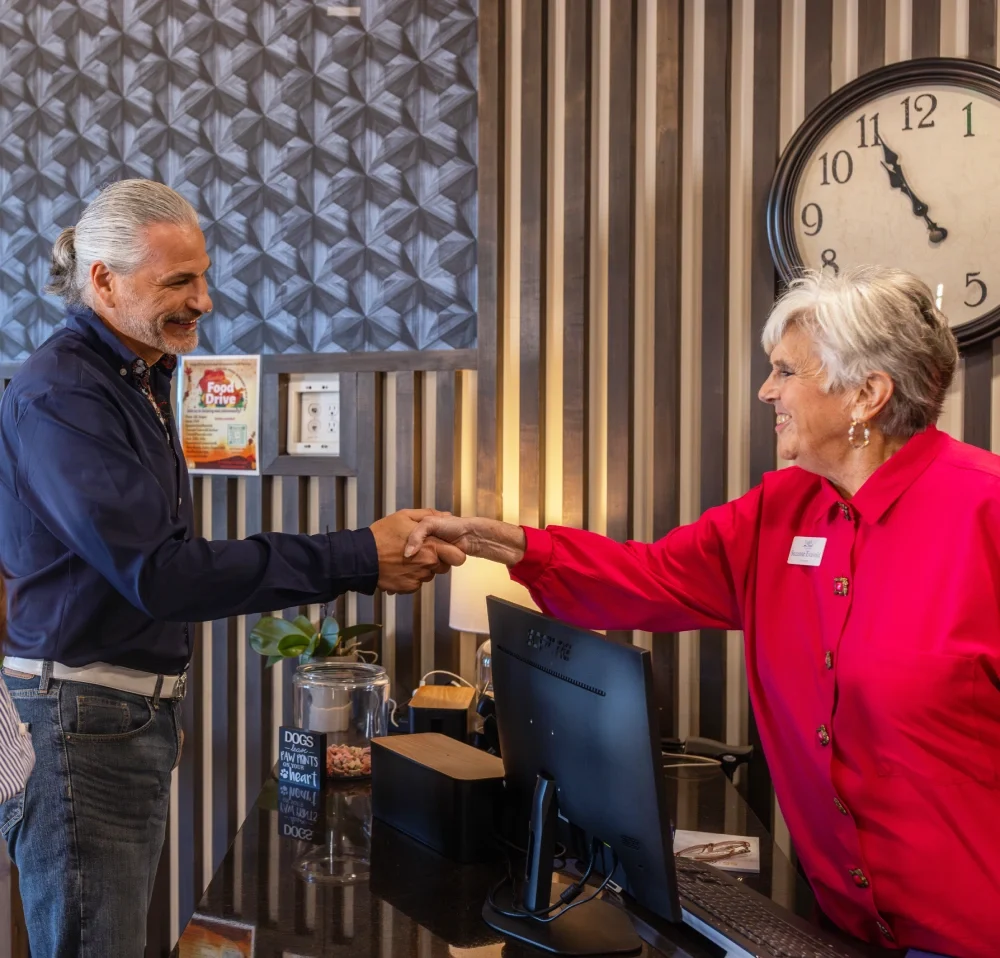 Man and a resident in a red shirt shaking hands in front of a wall clock