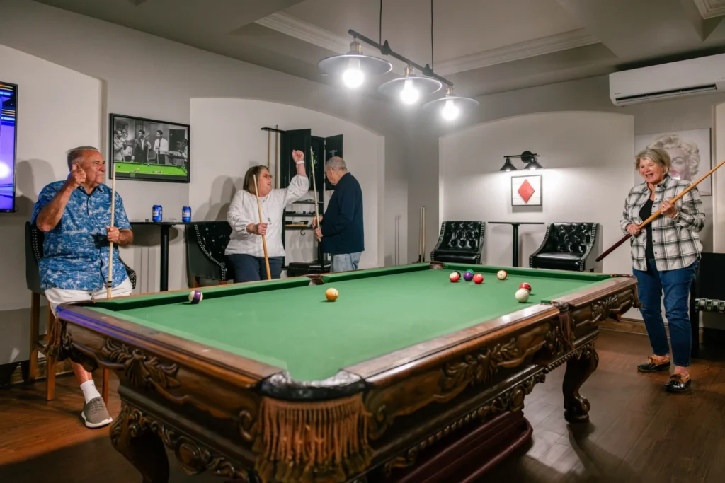 Mon Abri residents gather around a large green billiards table with pool cues.