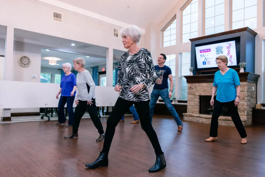 Mon Abri group practices dance steps beside the stone fireplace in the community room.