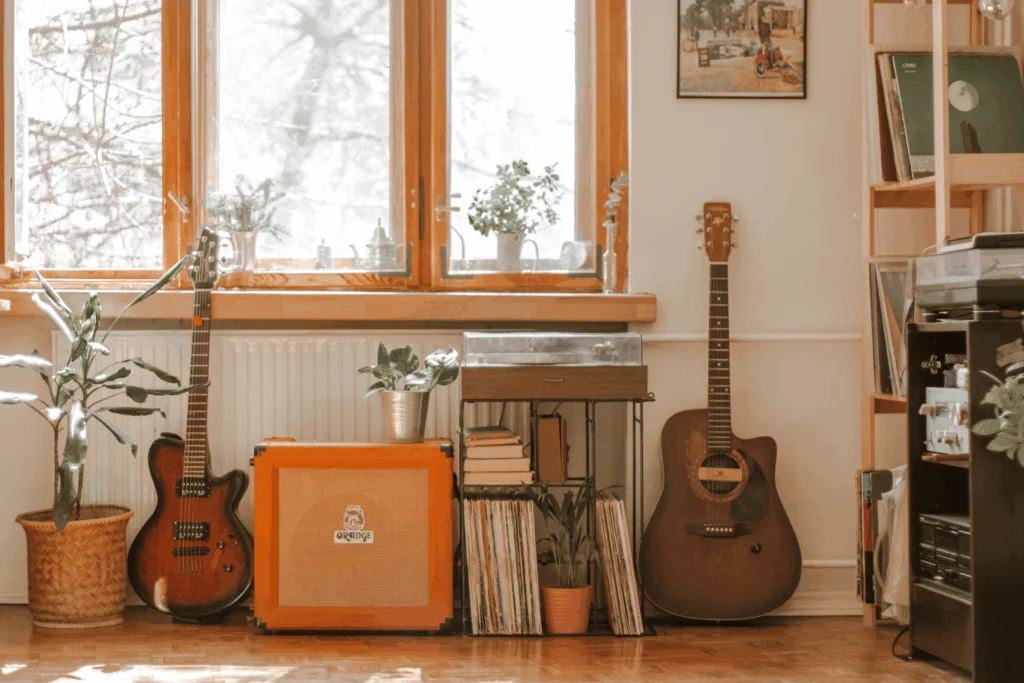 Music room corner with acoustic guitars, an orange amplifier, records and plants by a window
