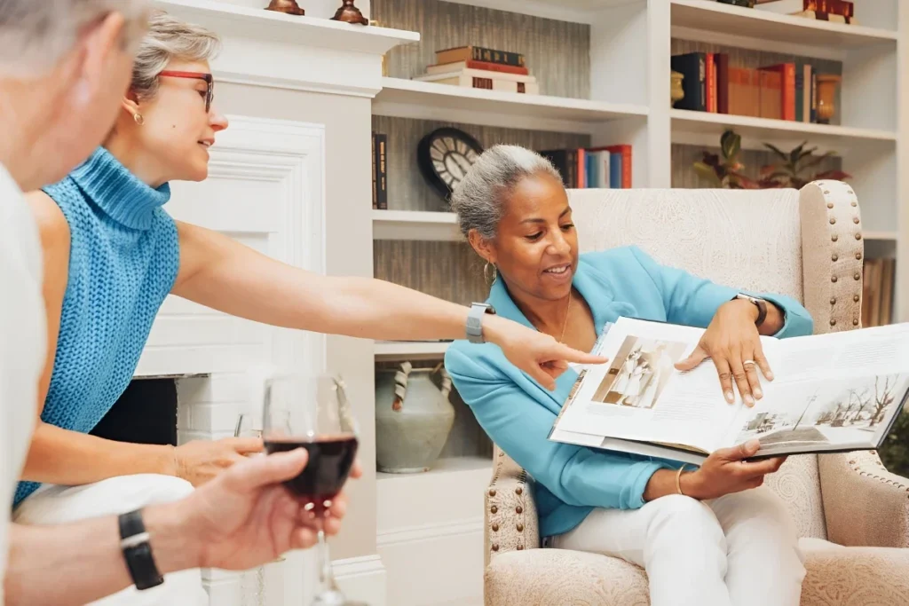 Senior adults looking through a photo album together in a living room with built-in bookshelves