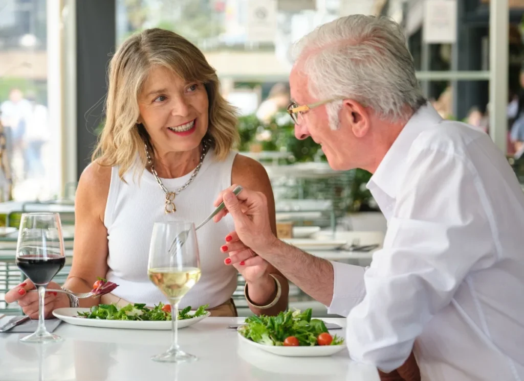 Senior couple enjoying salads and wine at an outdoor restaurant table
