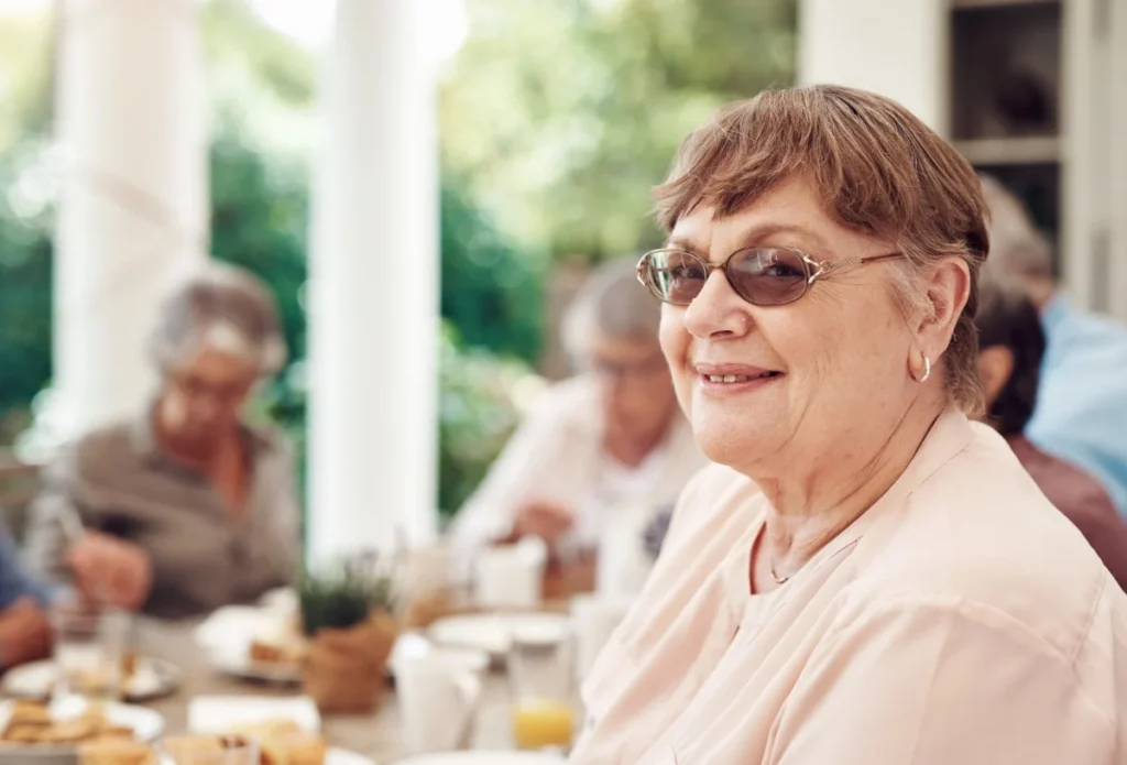 Smiling senior woman wearing sunglasses seated at a group dining table