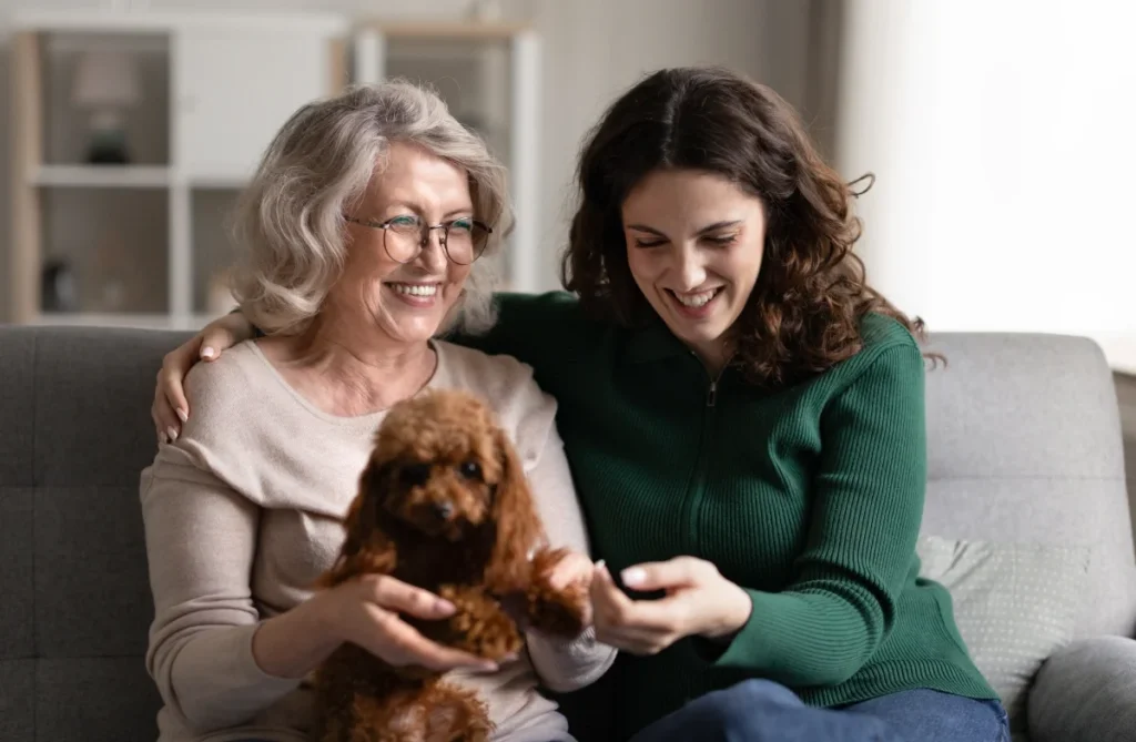 Granddaughter and senior grandmother laughing together on a couch with their dog