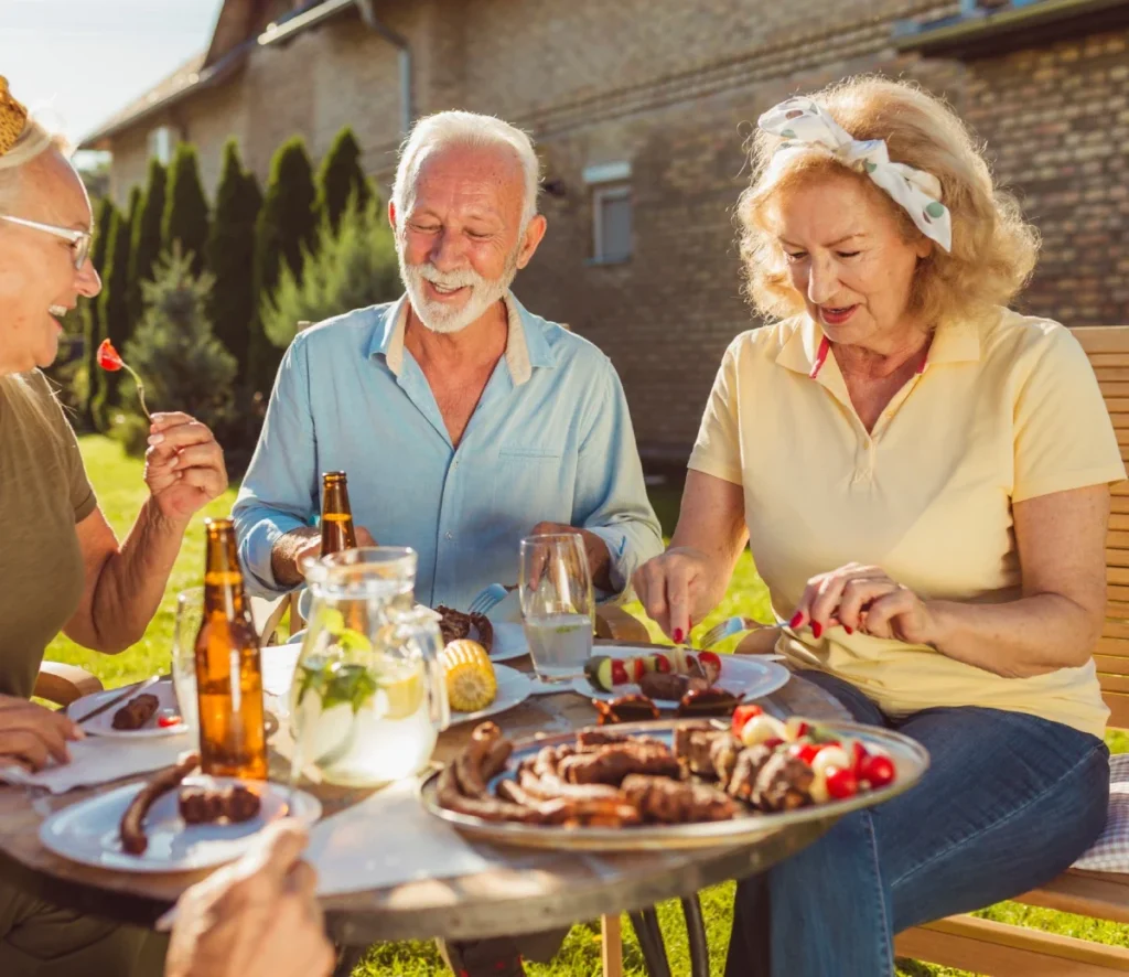 Group of seniors sharing a meal of grilled food and drinks at an outdoor table