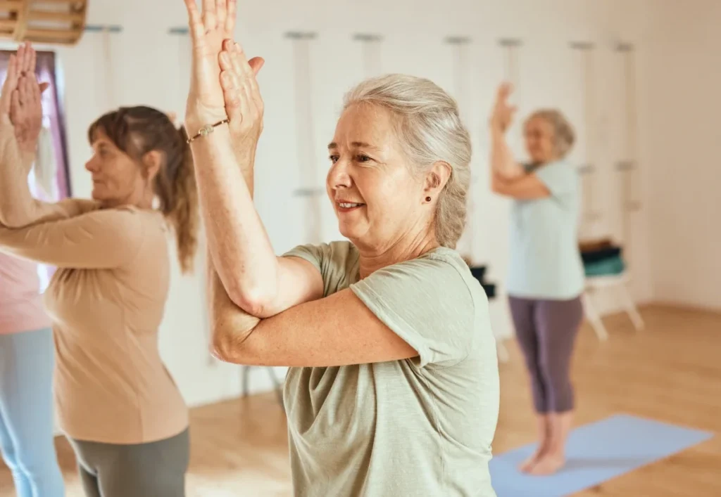Seniors practicing yoga in a bright studio with hands together overhead