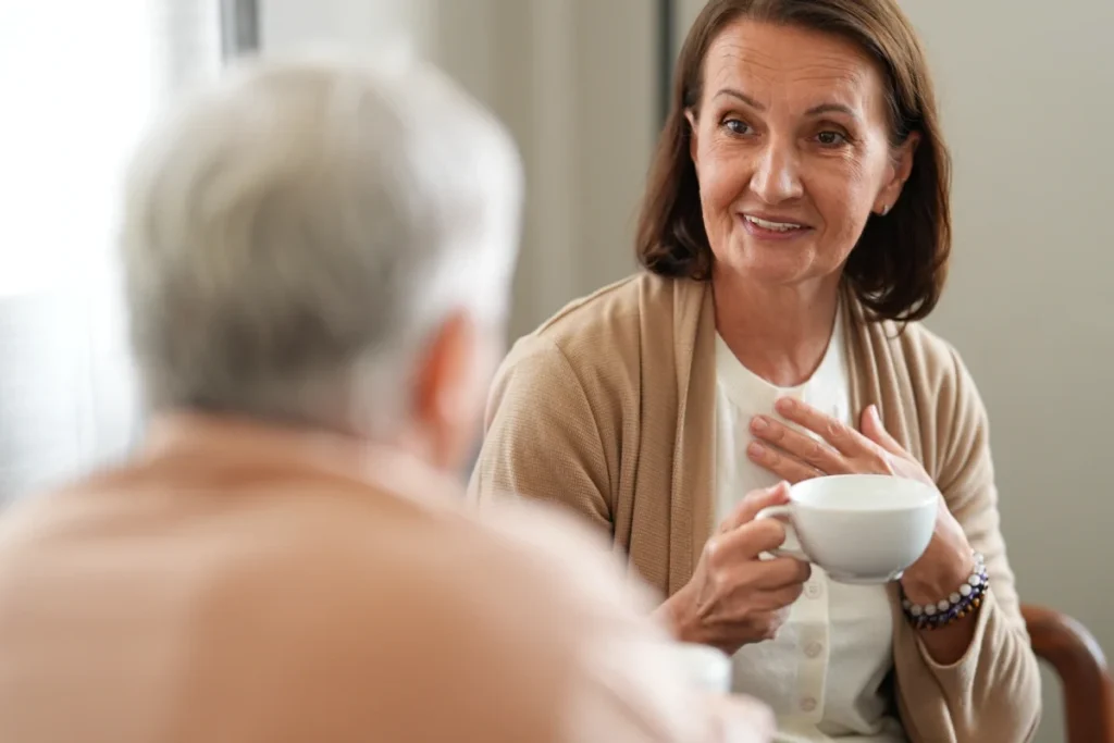 Senior woman smiling over a cup of coffee while talking with a man at a table
