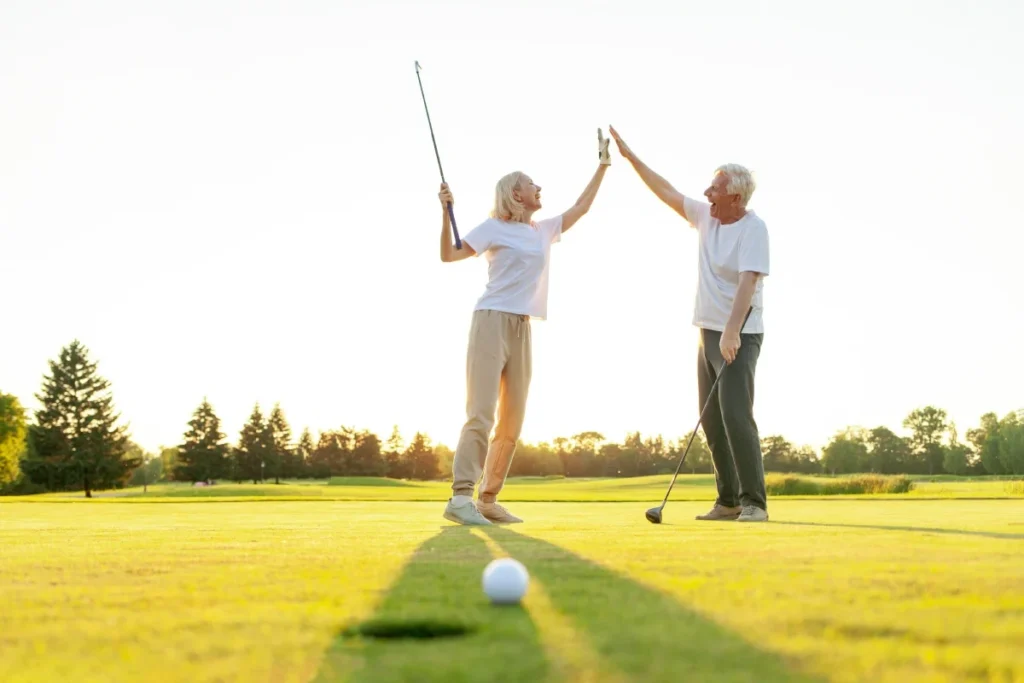 Two golfers celebrating with a high five on a sunlit putting green
