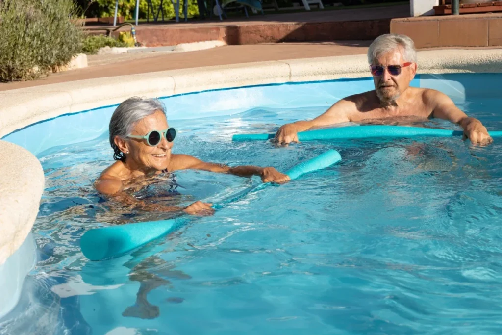 Senior man and woman doing a water workout with foam noodles in a pool