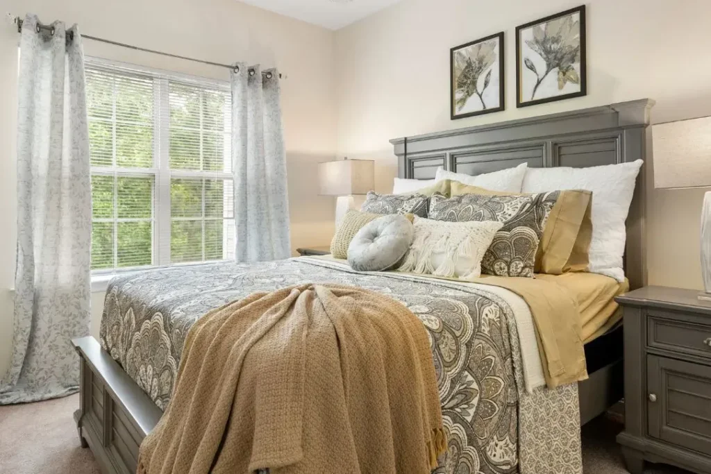 Bedroom with a gray headboard, a gold bedspread and patterned throw, and framed pictures above the bed