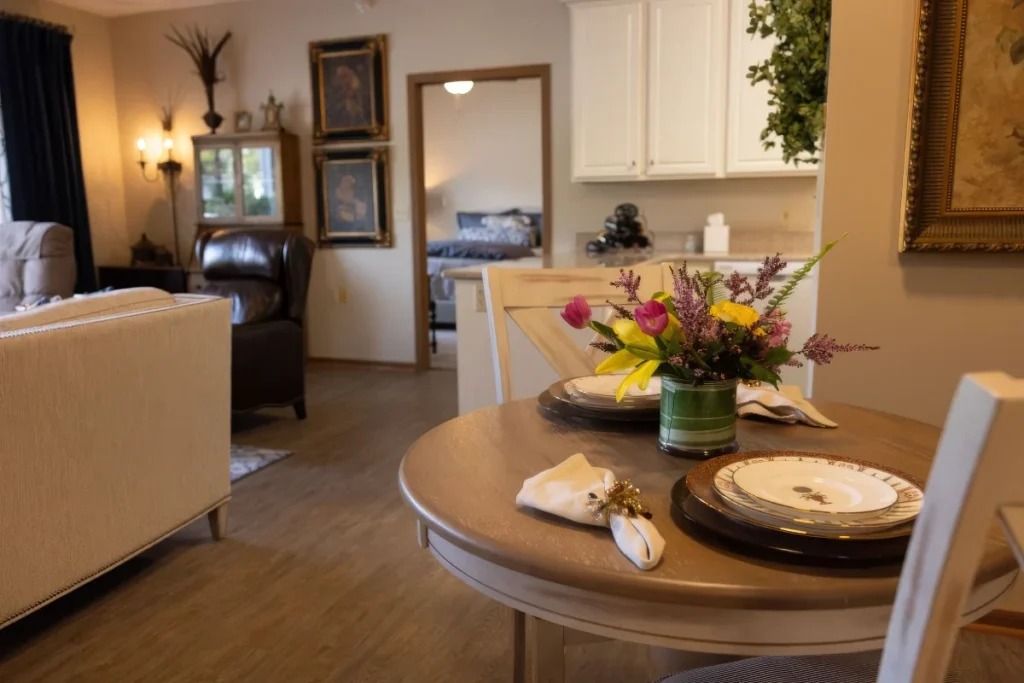 Dining table set with plates and a bouquet of flowers, with a living area and a framed mirror beyond