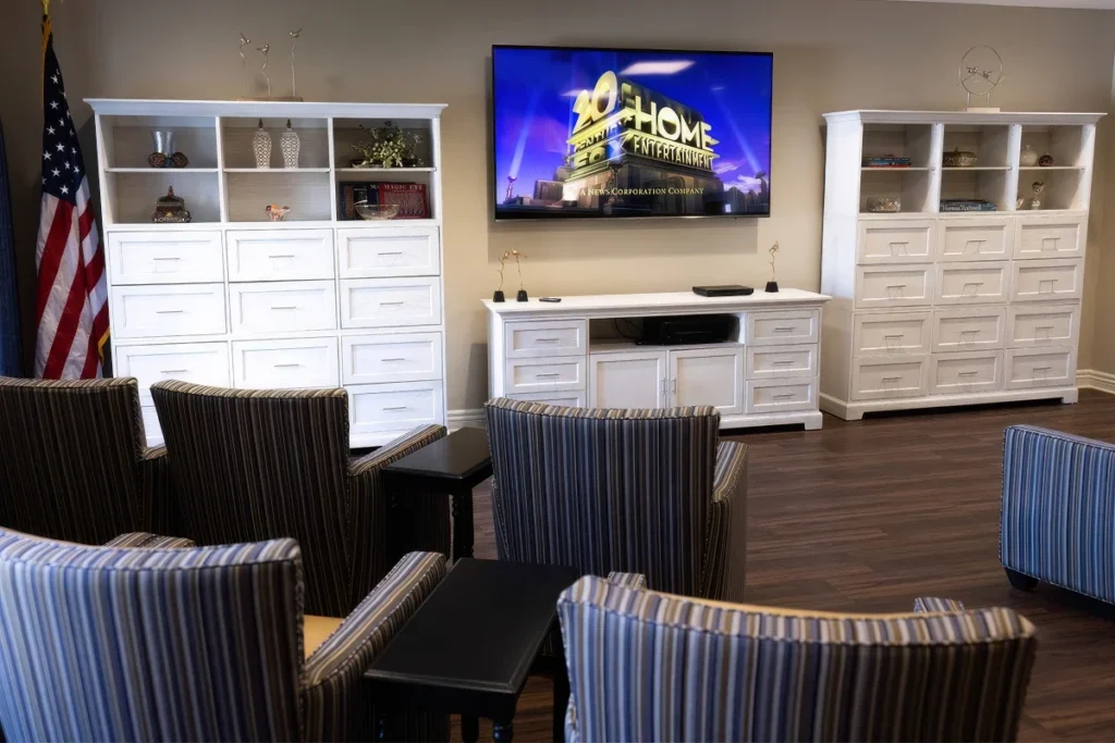 Lounge with striped armchairs, white cabinets and a wall-mounted TV, with an American flag at the side