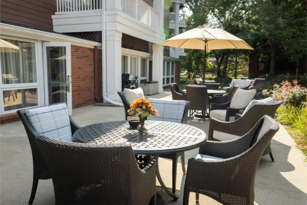 Outdoor patio with a round table with an umbrella and wicker chairs beside a brick building