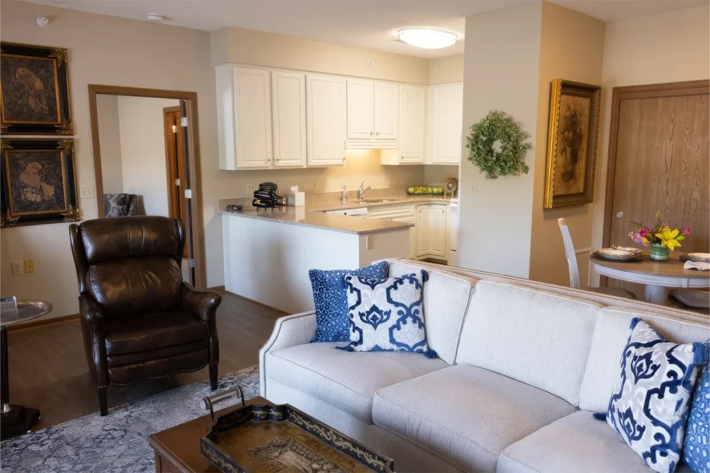 Apartment living area with a white sofa, a leather recliner and an open kitchen behind