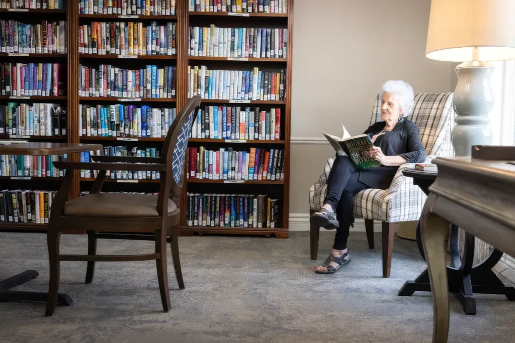 Older woman reading a book in an armchair in a library with tall bookcases