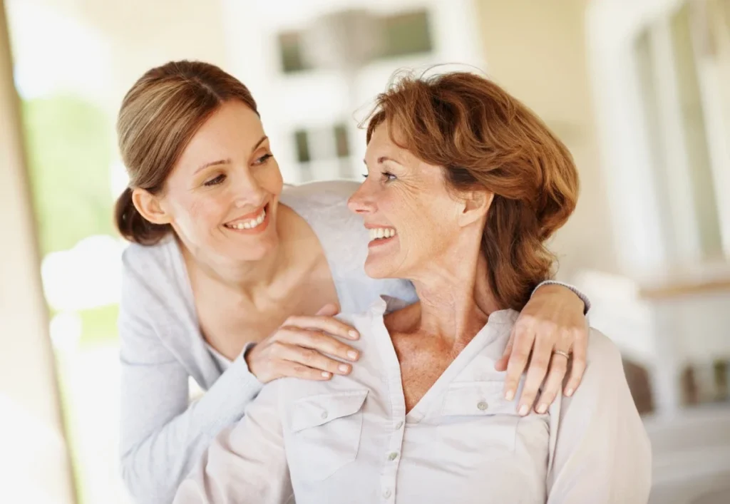Smiling caregiver with her arm around an older woman, both laughing