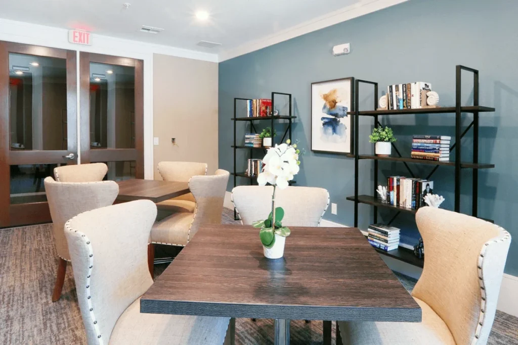 Dining table with cream upholstered chairs and a vase of flowers beside shelves of books, in a room with blue walls