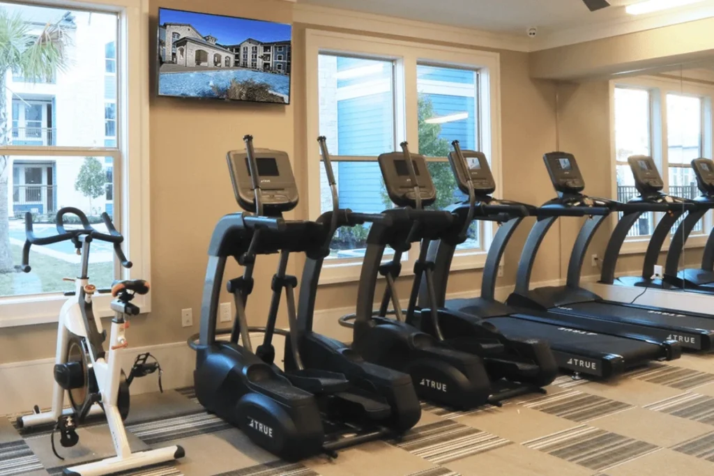 Fitness room with treadmills, ellipticals and a stationary bike, with a TV on the wall