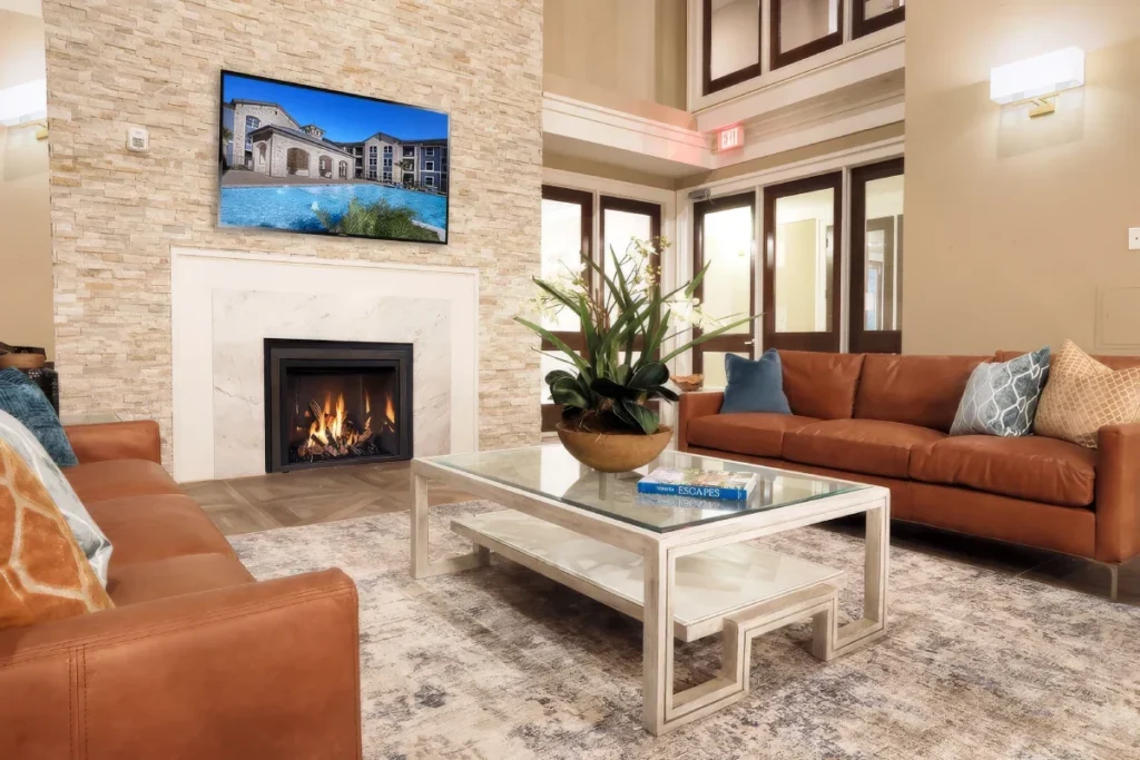 Lounge with a stone fireplace, leather sofas, a coffee table and a wall-mounted TV under a high ceiling