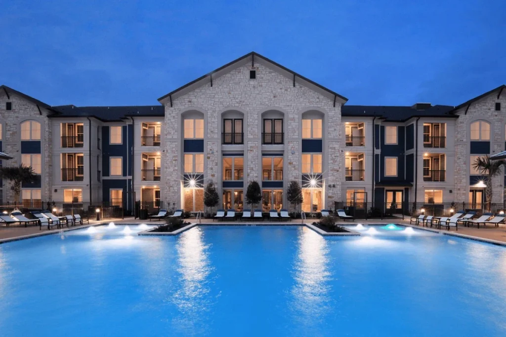 Swimming pool at dusk in front of a stone-and-brick apartment building with lit windows