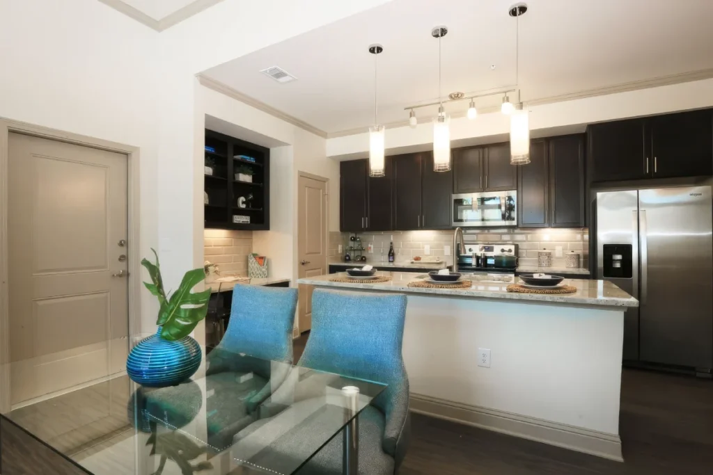 Kitchen with a large island, blue chairs, dark cabinets and pendant lights