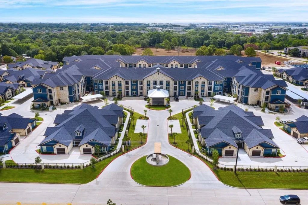 Aerial view of a large residential community with gray-blue roofs, a central lawn and tree-lined grounds