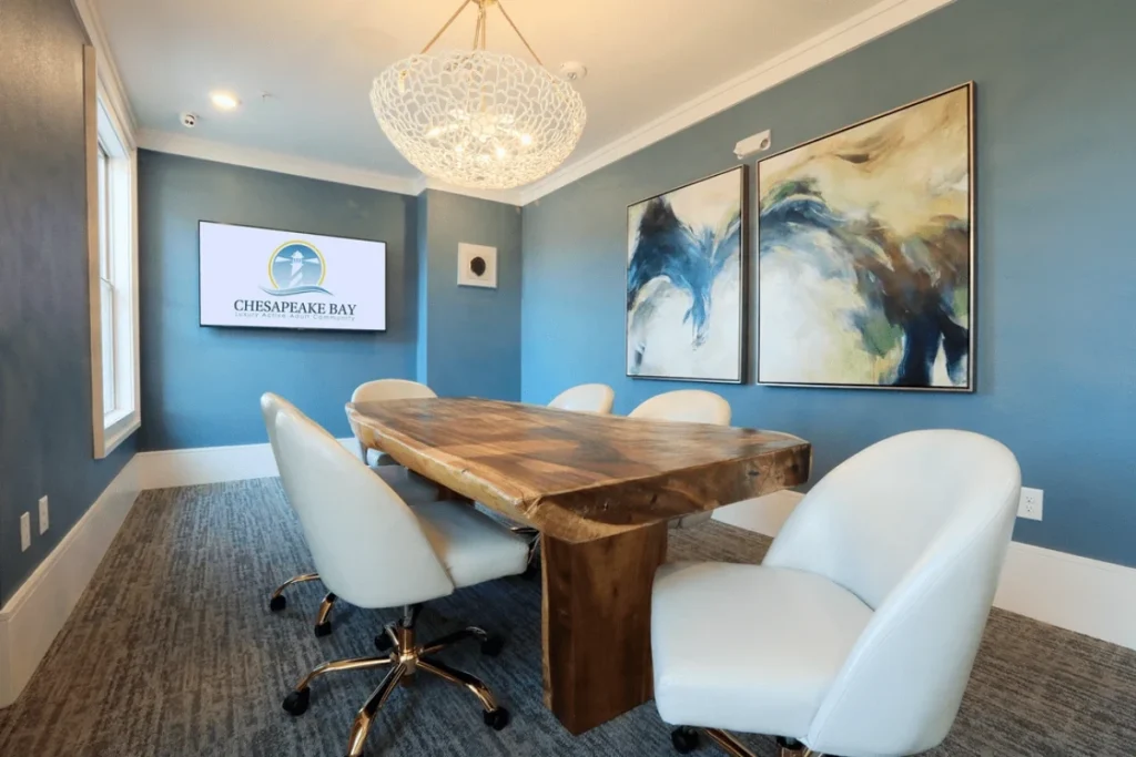 Meeting room with a live-edge wood table, white chairs, blue walls, abstract art and a wall-mounted screen