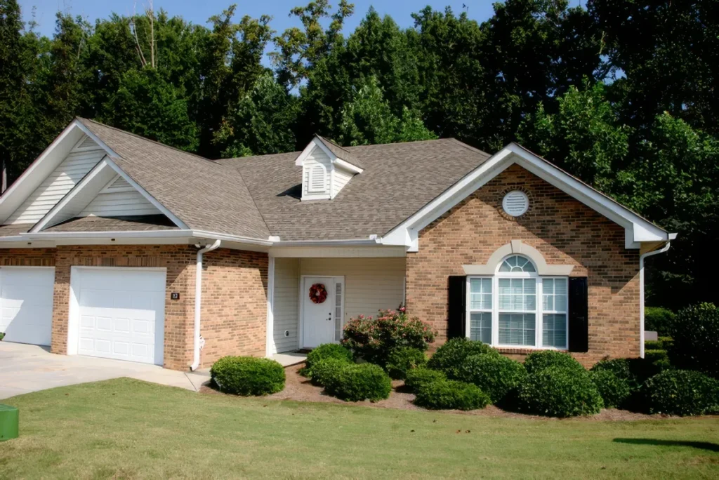 Brick home with a gabled roof, an arched window and white garage doors, with trimmed shrubs and a lawn