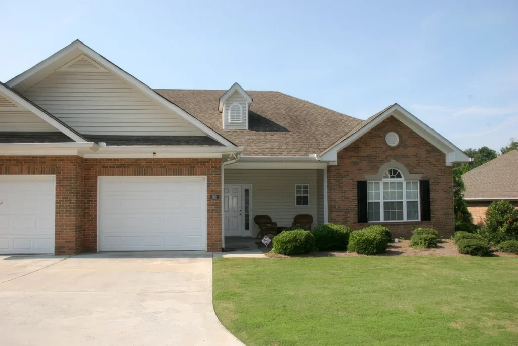Brick home with two white garage doors, a covered porch and a green lawn