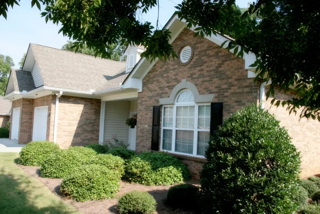 Brick home with an arched window and a rounded shrub, framed by tree branches