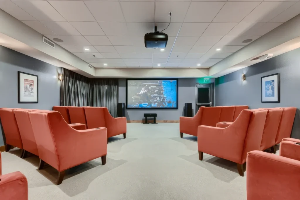 Theater-style lounge with orange armchairs facing a large screen and a ceiling projector