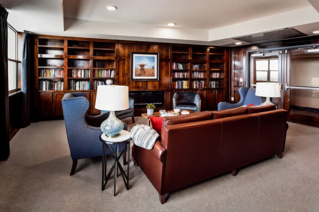 Library lounge with built-in wooden bookshelves, a leather sofa and blue armchairs