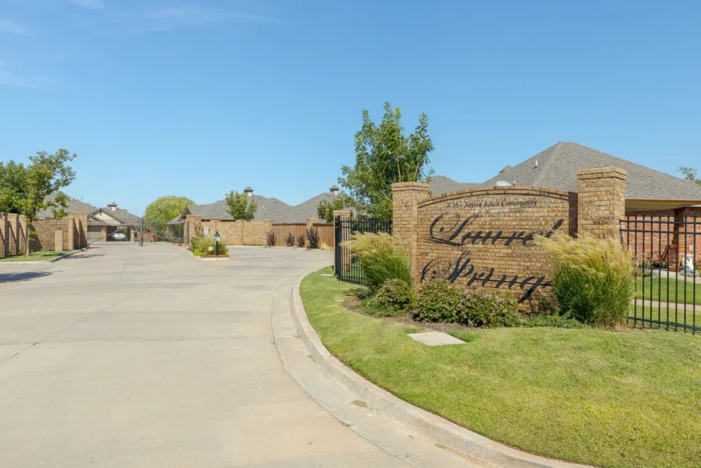 Stone entrance monument sign beside a paved road, with trees and homes in the background