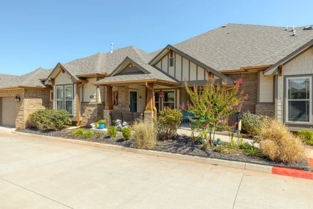 Row of single-story homes with peaked rooflines and landscaped beds along a driveway