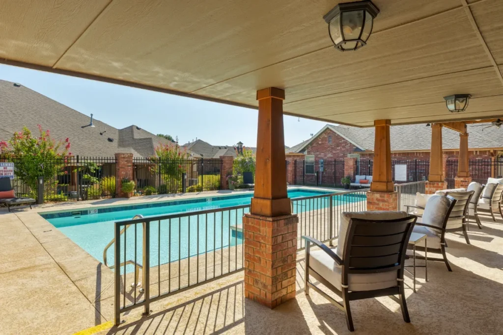 Covered patio with lounge chairs beside a fenced swimming pool
