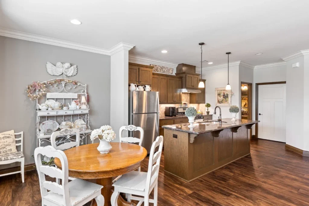 Kitchen with an island and white chairs at a round wooden dining table beside a white shelf