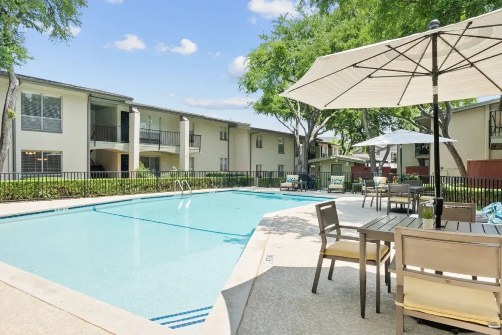 Outdoor pool with patio umbrellas and chairs, beside a two-story building