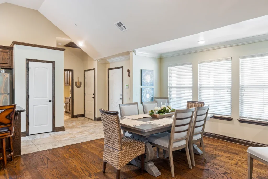 Dining nook with a wood table, six chairs and large windows with white blinds