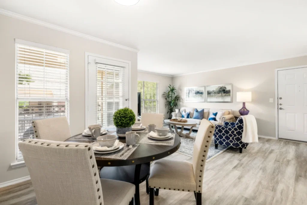 Apartment dining and living area with a table set for four, a sofa and large windows with blinds
