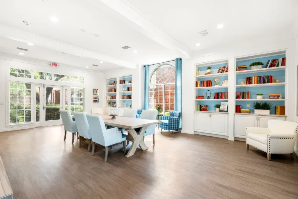 Sunny library and dining room with built-in bookshelves, light blue chairs and a long table
