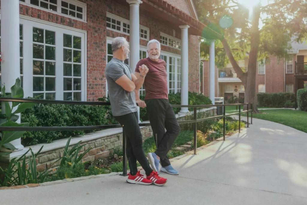 Two older adults in workout clothes chatting on a walkway beside a brick building