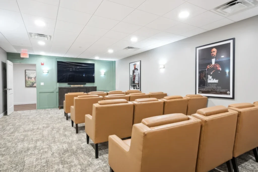 Movie room with rows of tan leather recliners facing a wall-mounted TV and a framed poster