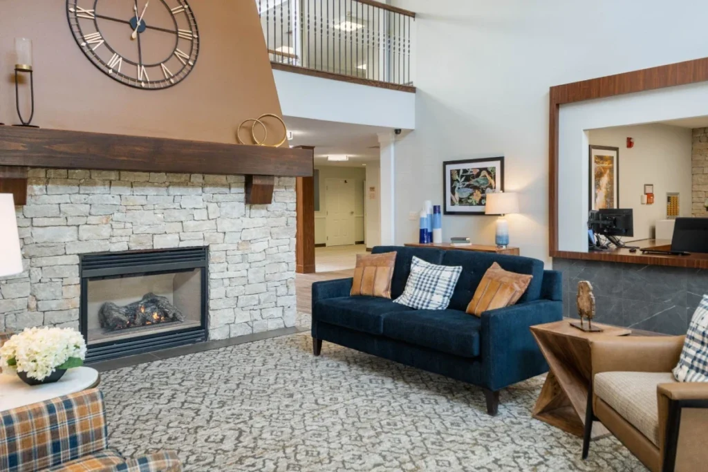 Lounge with a stone fireplace, a navy sofa, armchairs and a large wall clock
