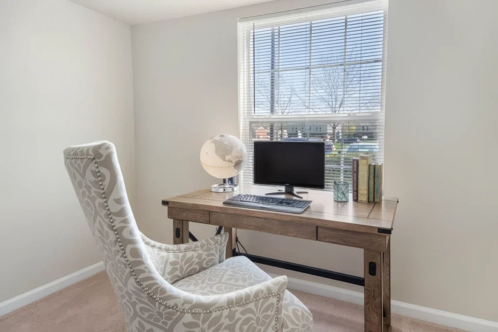 Small office corner with a wooden desk, a computer monitor and a patterned armchair by a window