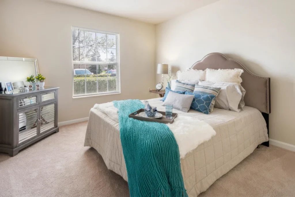 Bedroom with a gray headboard, white bedding and a teal throw, with a window and dresser