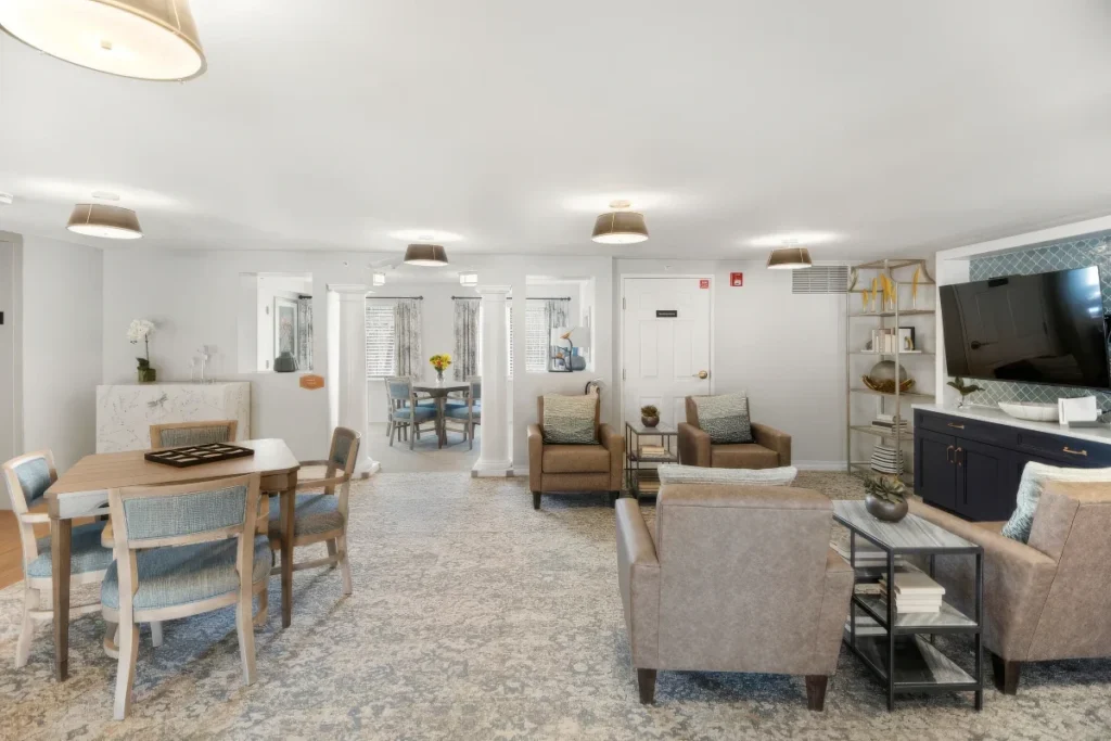 Lounge and activity area with armchairs, a table and a wall-mounted TV